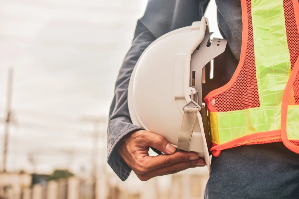 Industrial worker wearing a high-visibility safety vest and holding a hard hat.